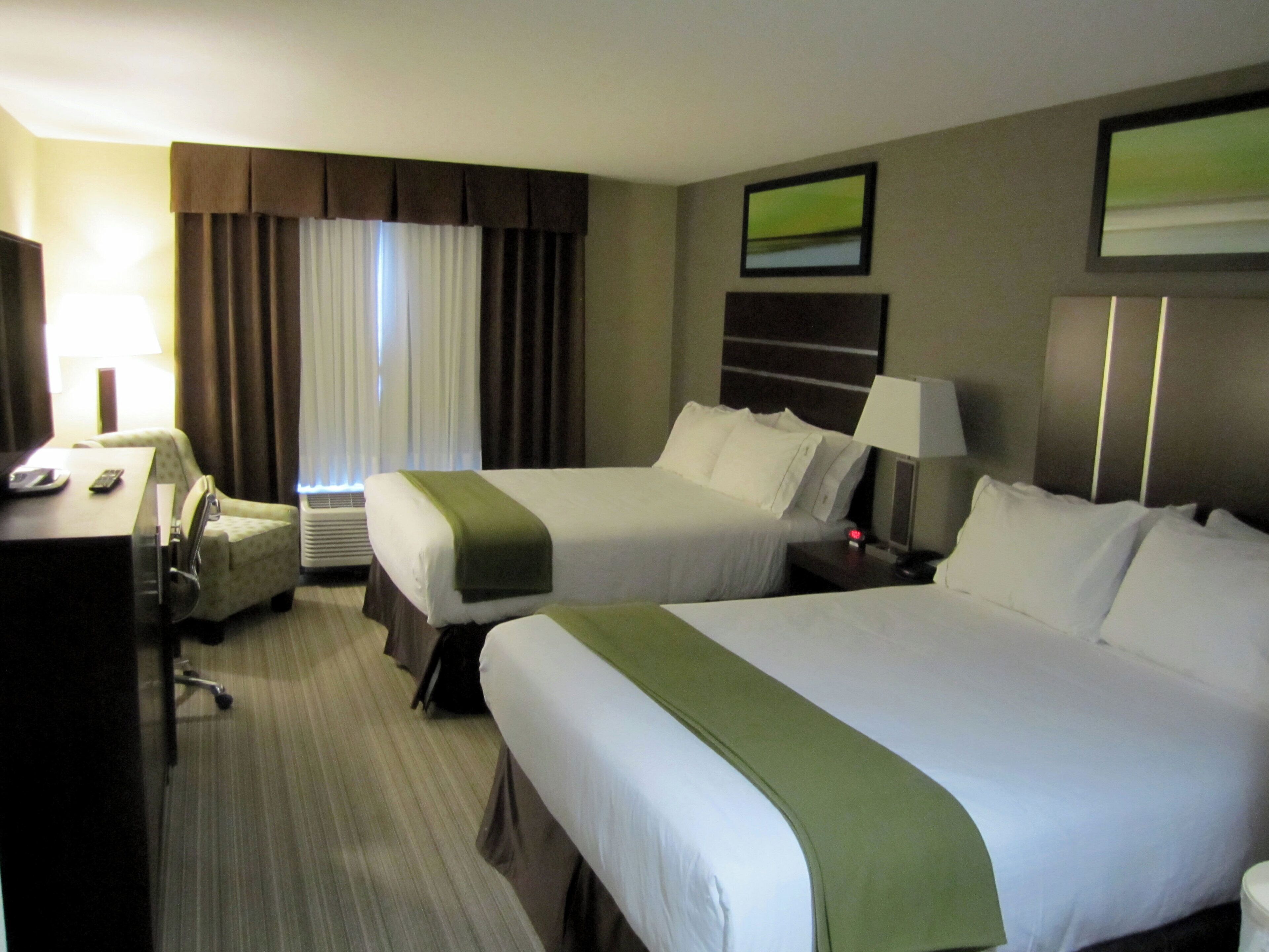 Ein Hotelzimmer mit zwei Betten, einem Schreibtisch, einem Stuhl, einer Lampe und einem Fernseher.