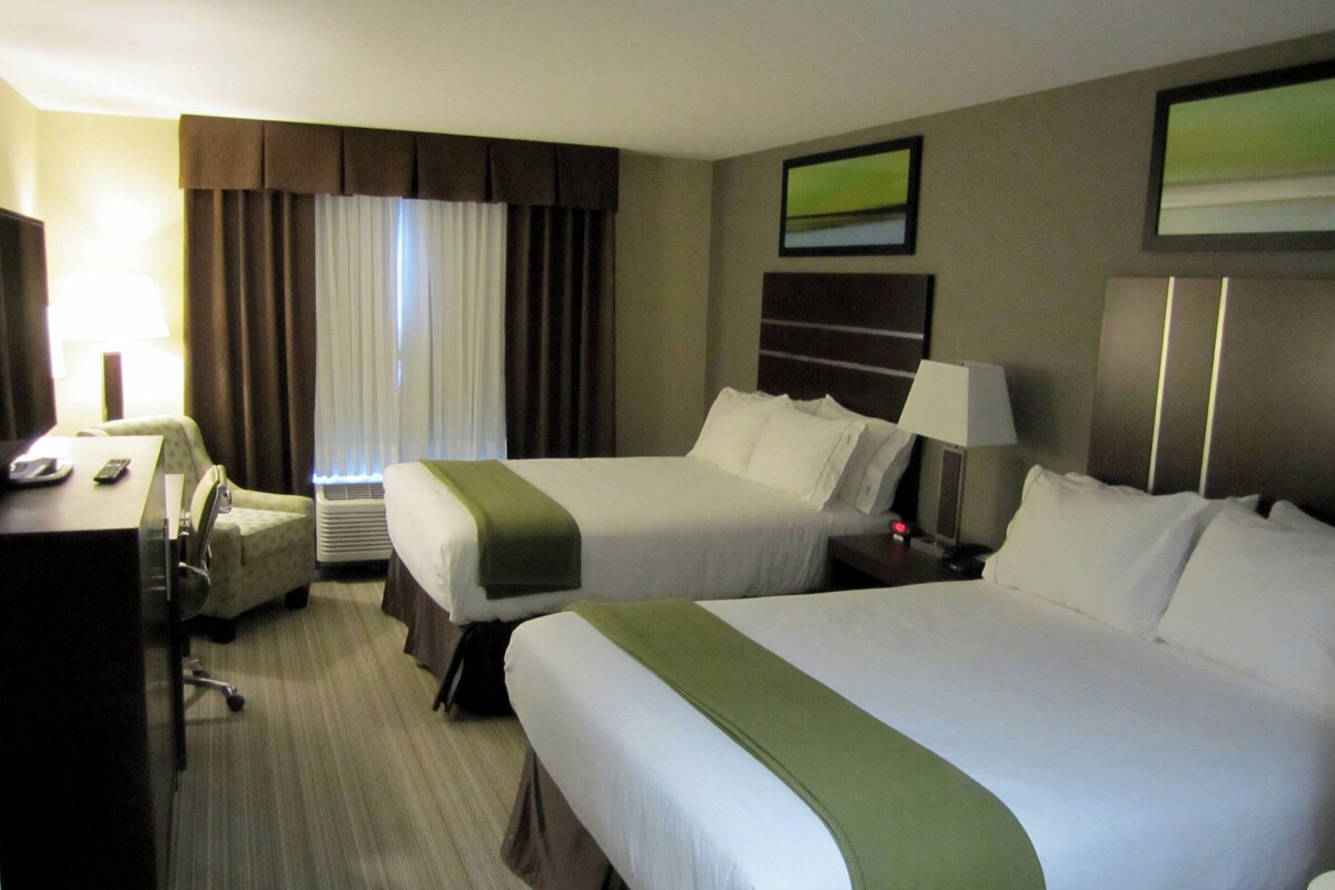 A hotel room with two beds, a desk, a chair, a lamp, and a television.
