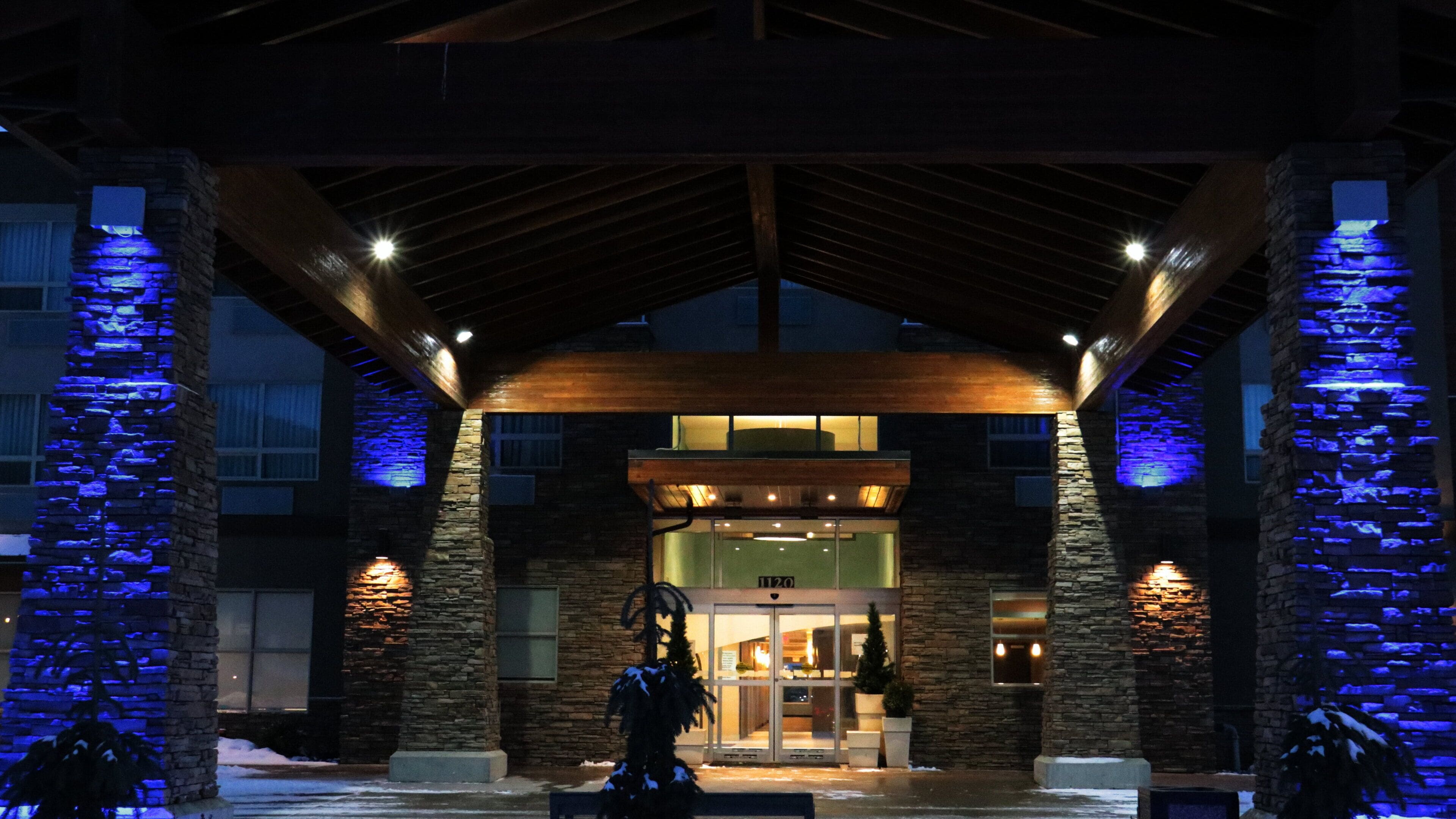 Fachada de piedra, vigas de madera y luces azules iluminadas en la entrada de un edificio.