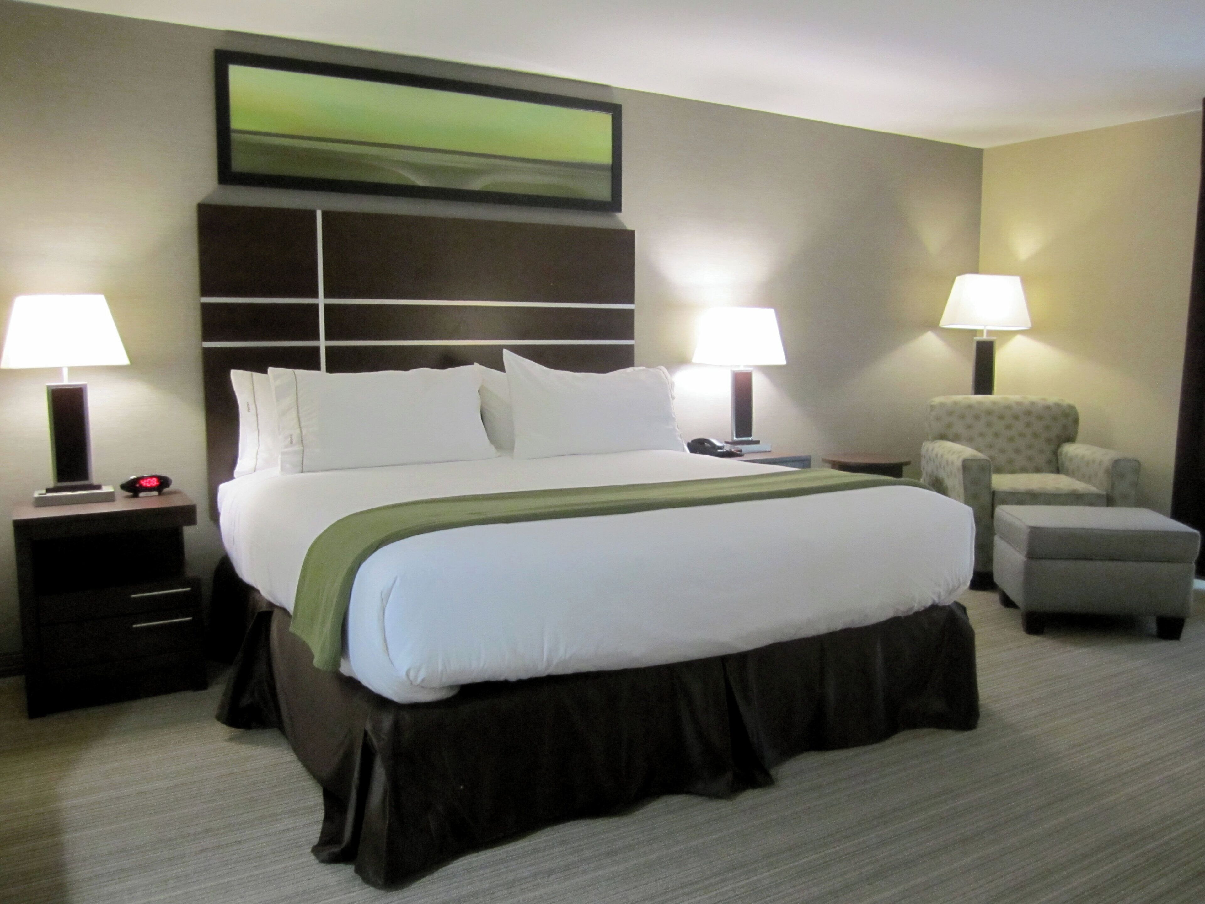Une chambre d’hôtel avec un grand lit, deux tables de chevet, une chaise et une lampe.