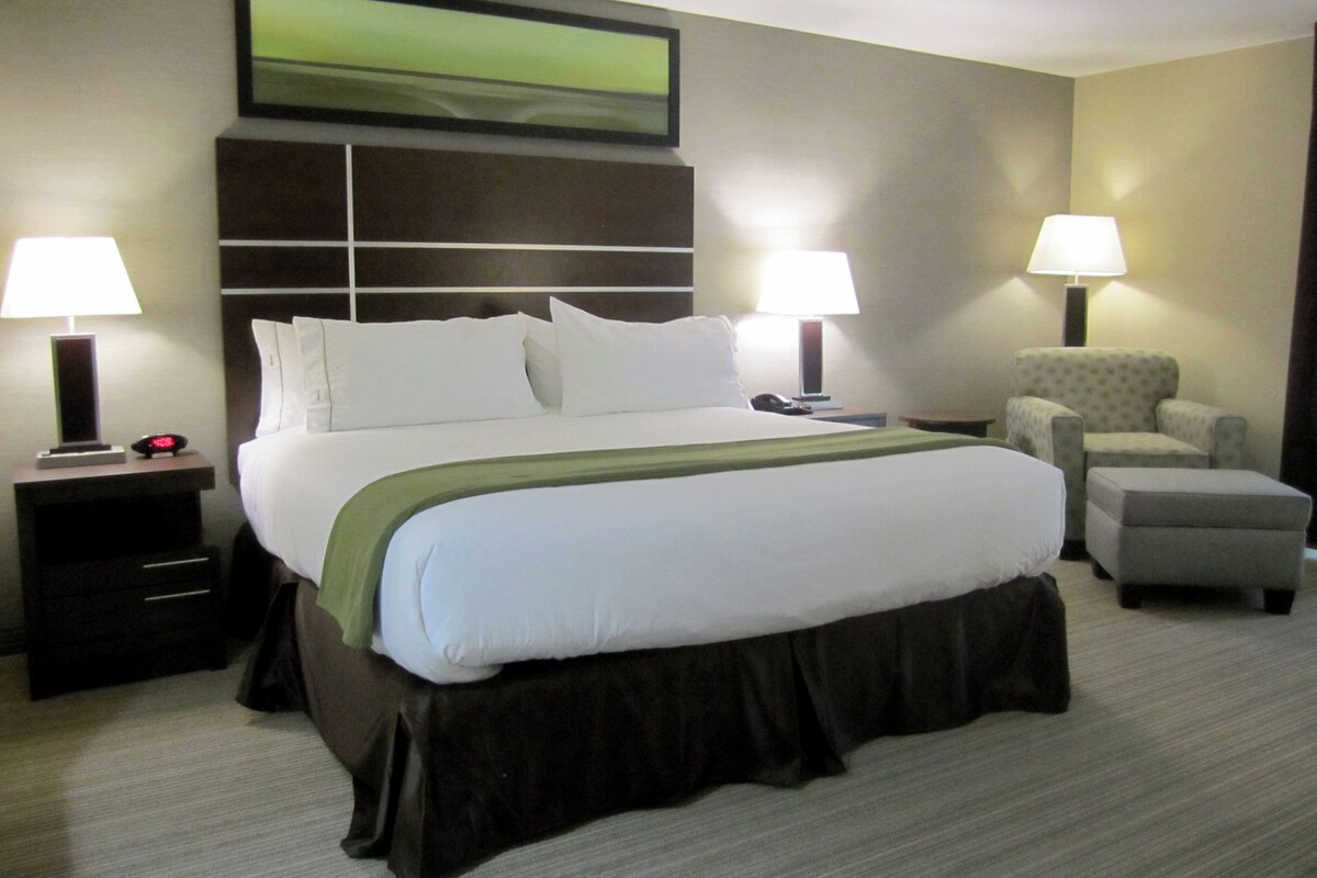 A hotel room with a large bed, two bedside tables, a chair, and a lamp.