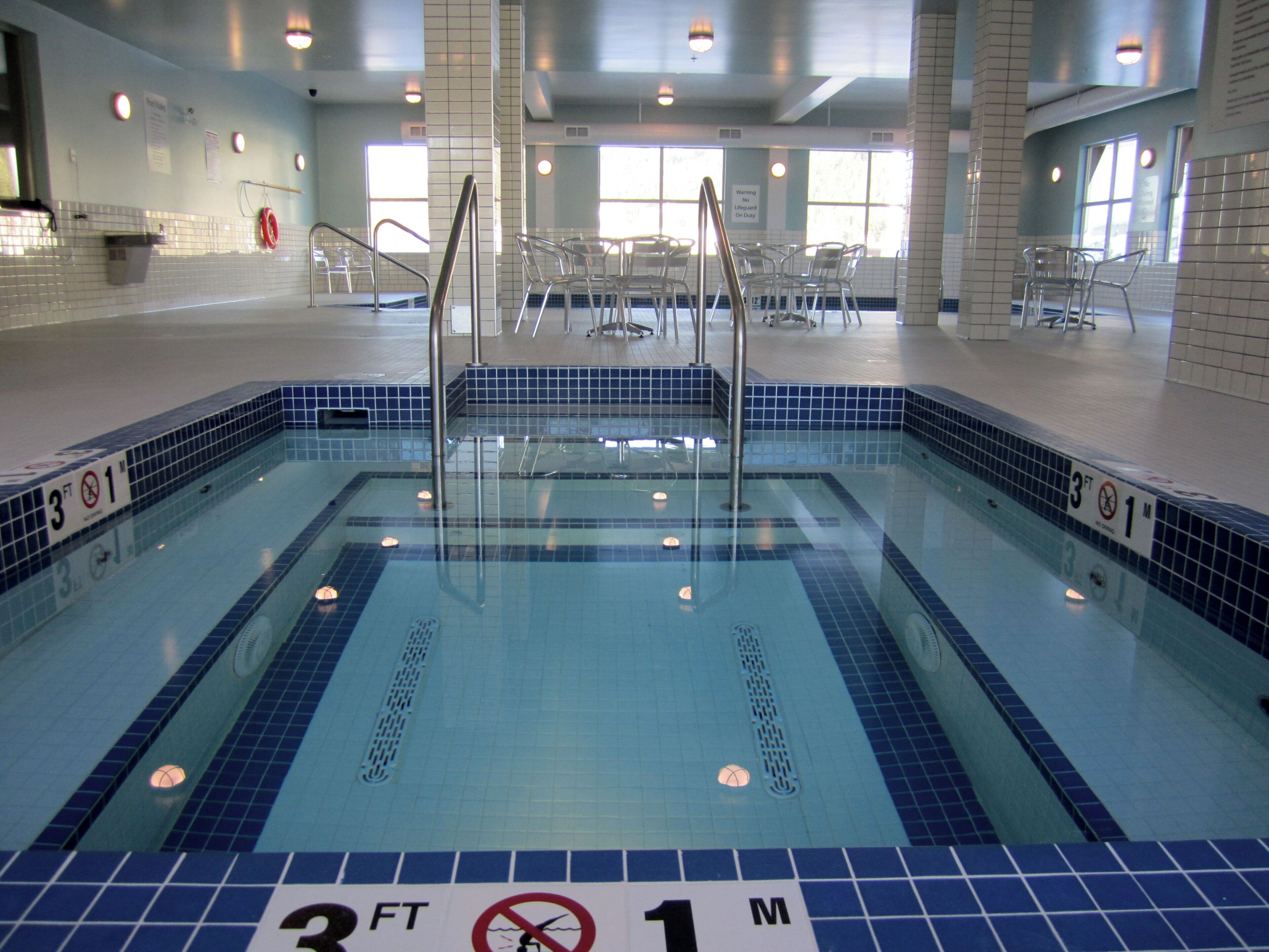 An indoor swimming pool with clear water, marked depth indicators, and a tiled border.