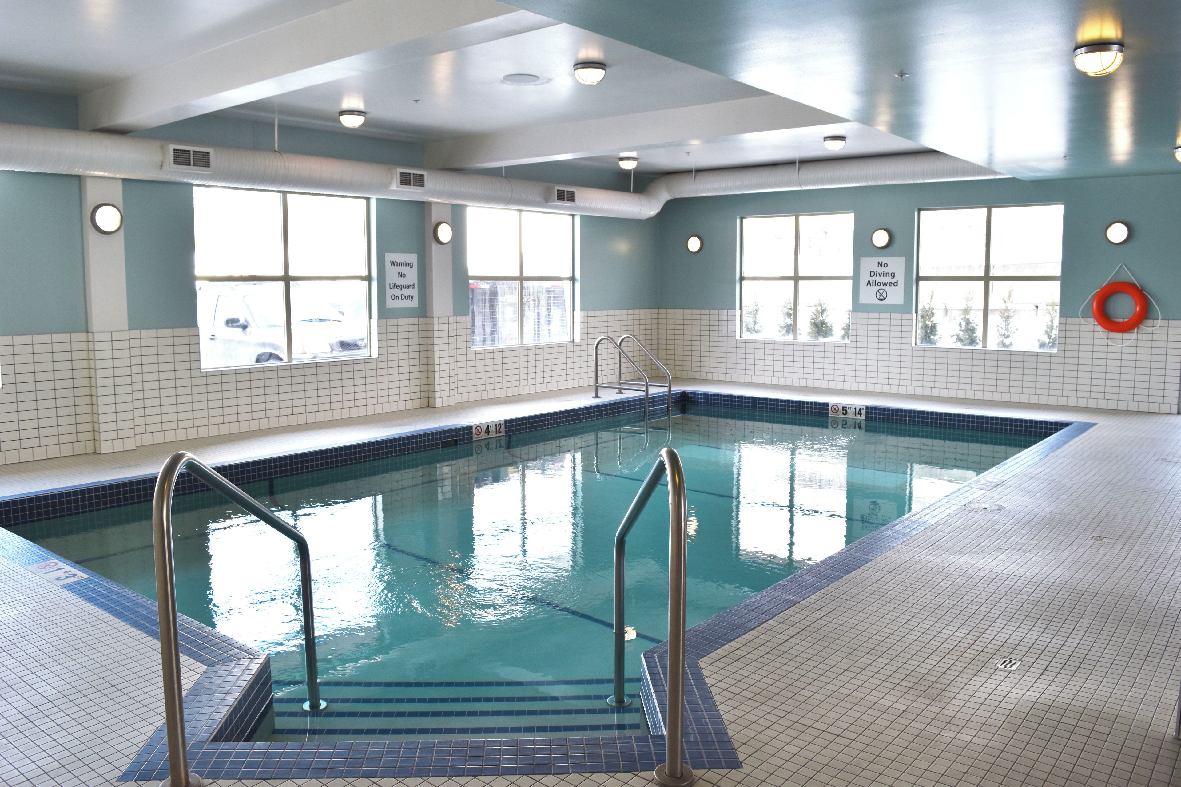Une piscine intérieure à l’eau claire, avec des murs carrelés et des fenêtres.