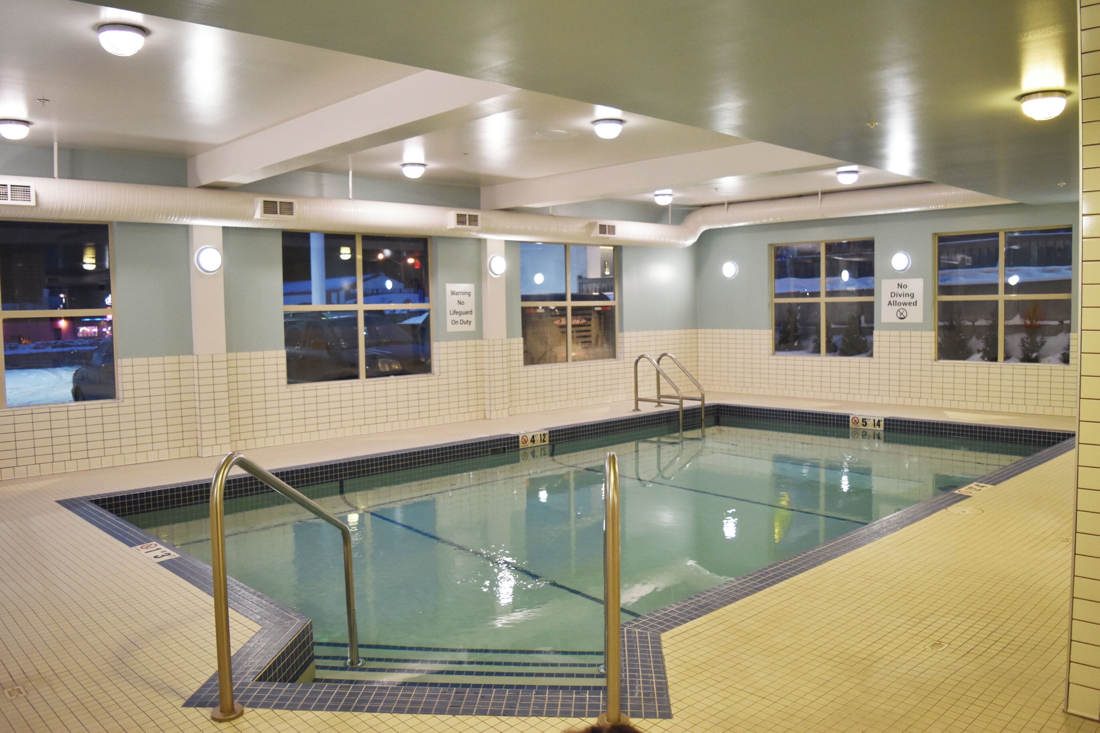 Una piscina interior con paredes de azulejos, ventanas y un cartel de socorrista.