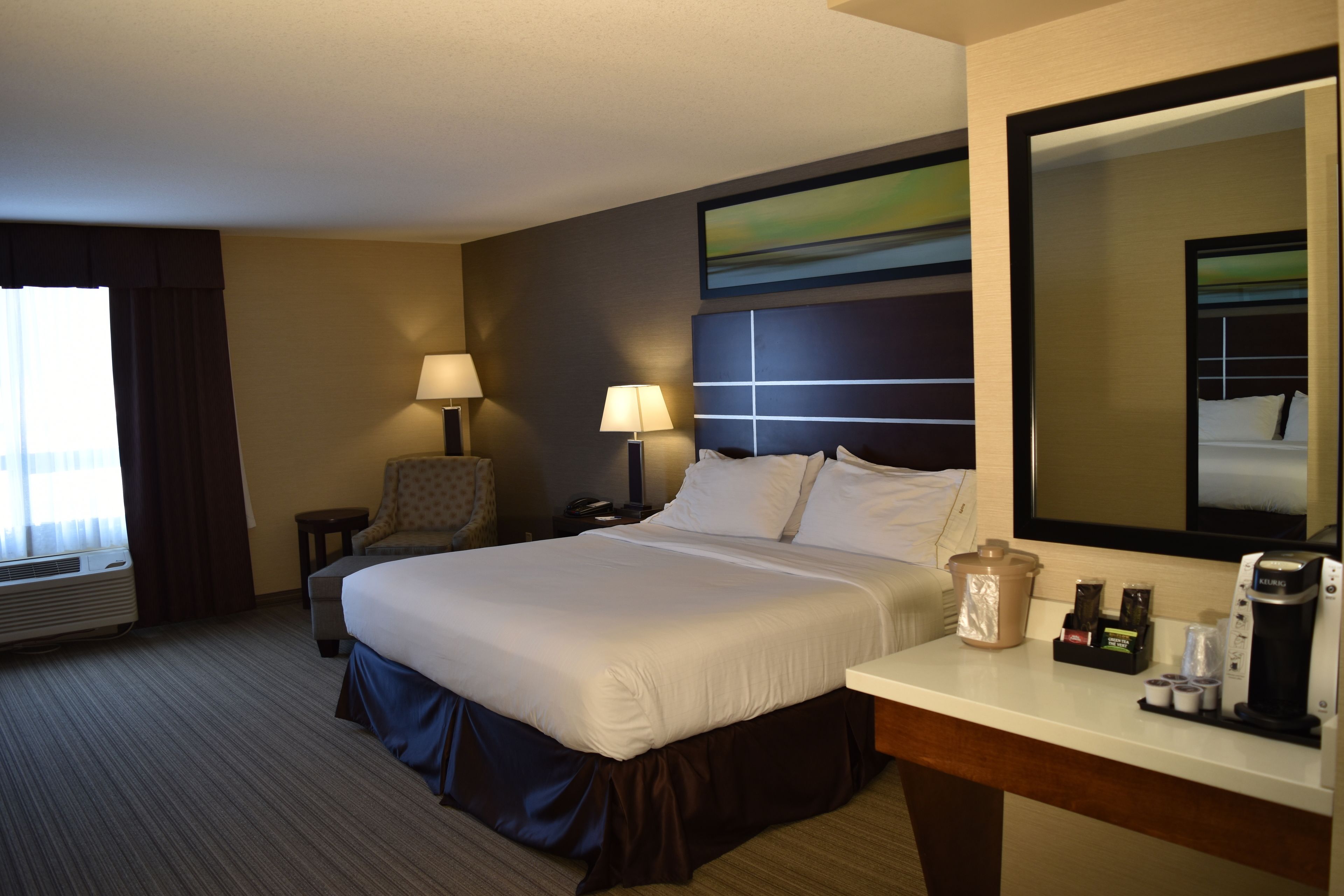 A hotel room with a large bed, bedside tables, a desk with a coffee maker, and a chair.
