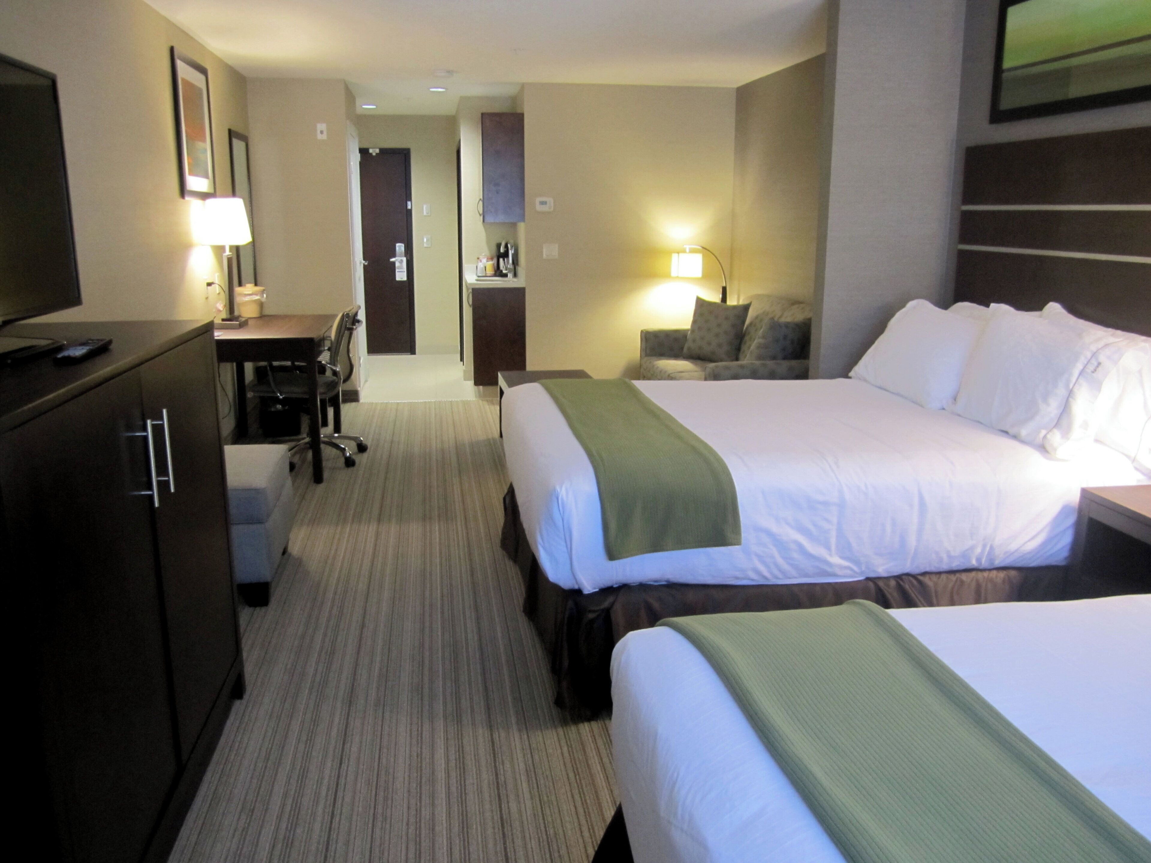 Habitación de hotel con dos camas, un escritorio, una silla y un televisor.