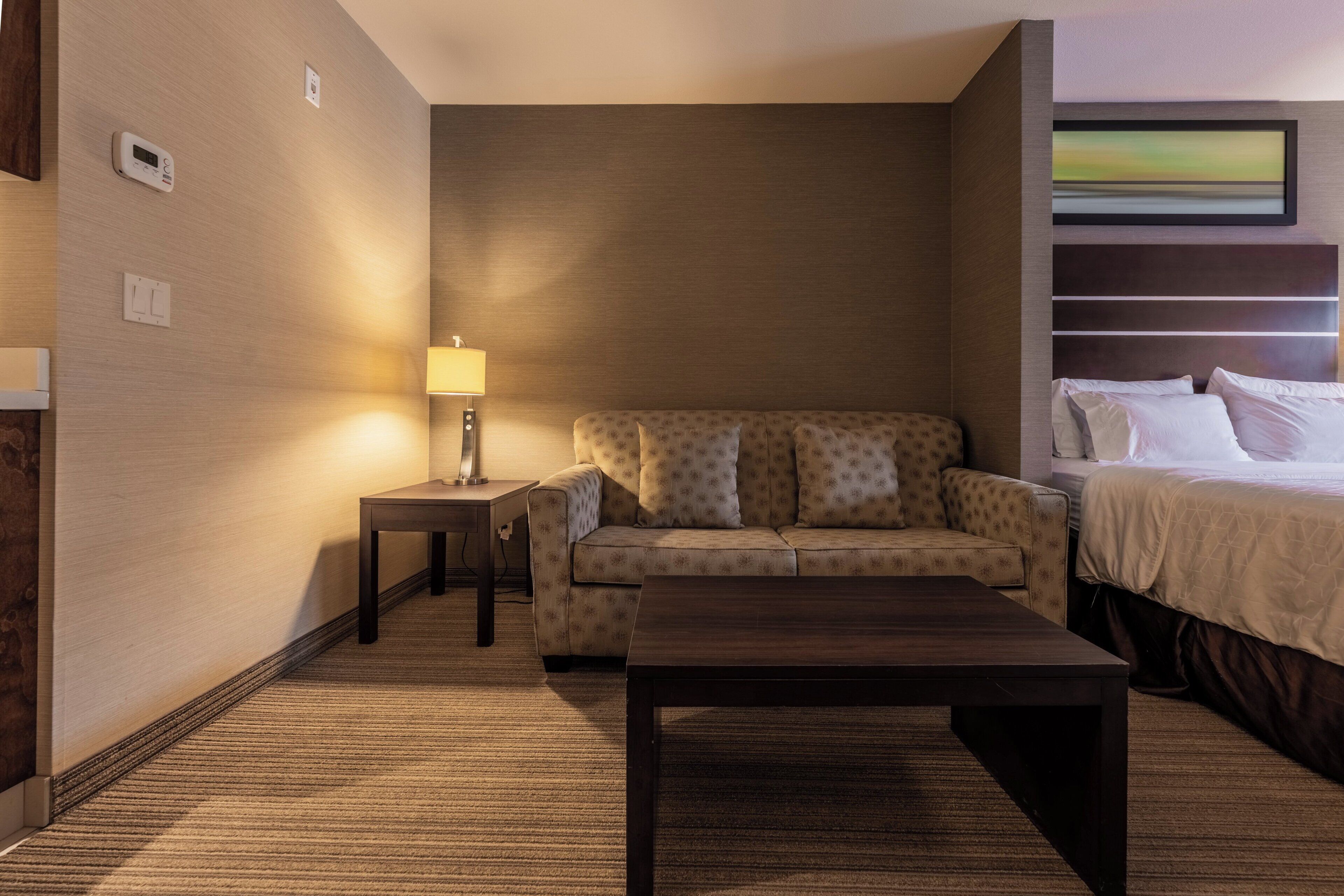 Una habitación de hotel con una cama, un sofá, una mesita, una lámpara y un cuadro en la pared.
