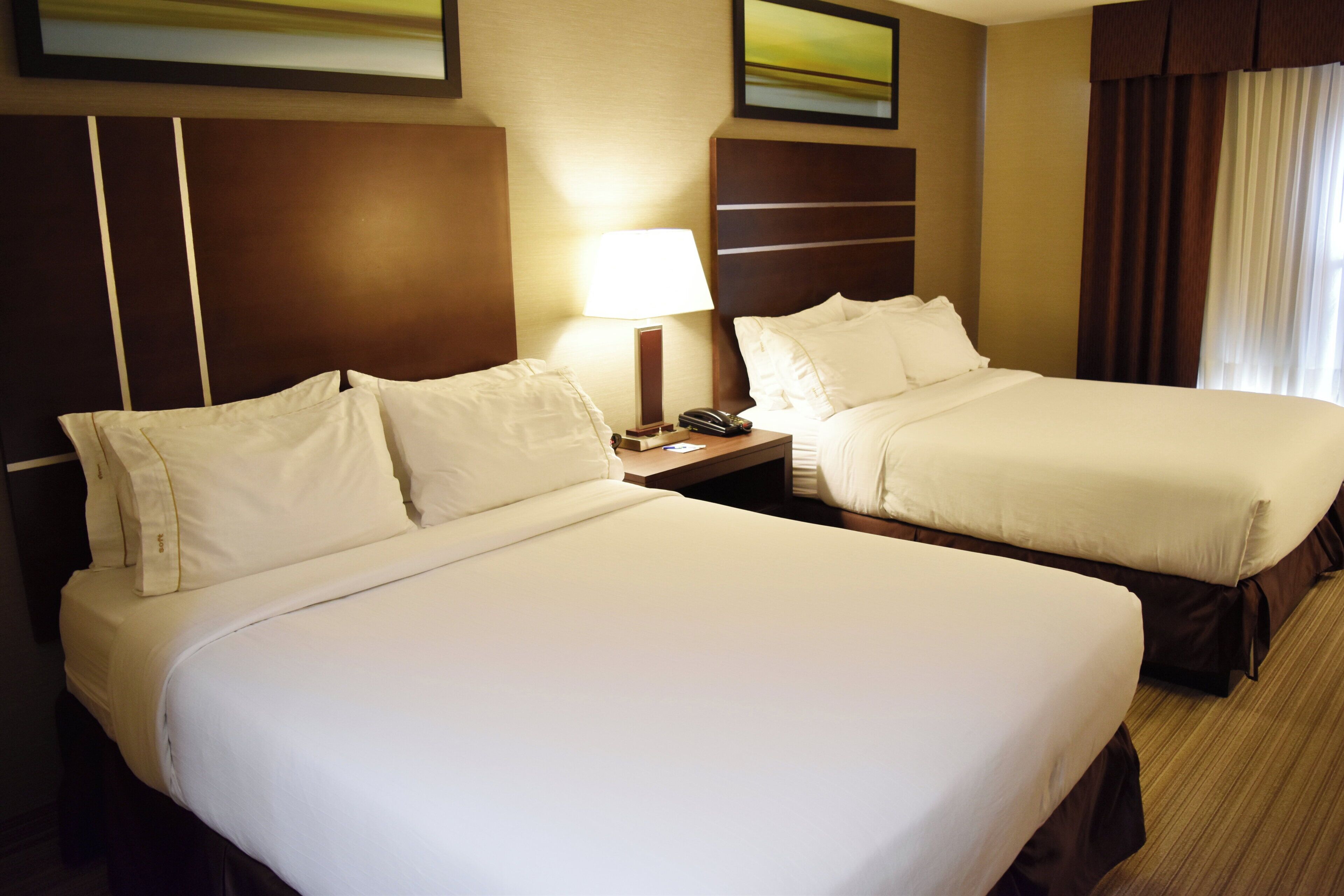 A hotel room with two beds, a nightstand with a lamp, and a painting on the wall.