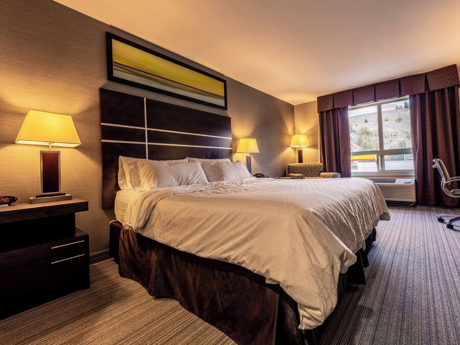 Quarto de hotel com uma cama grande, duas mesas de cabeceira, uma escrivaninha, uma cadeira e uma janela com cortinas.