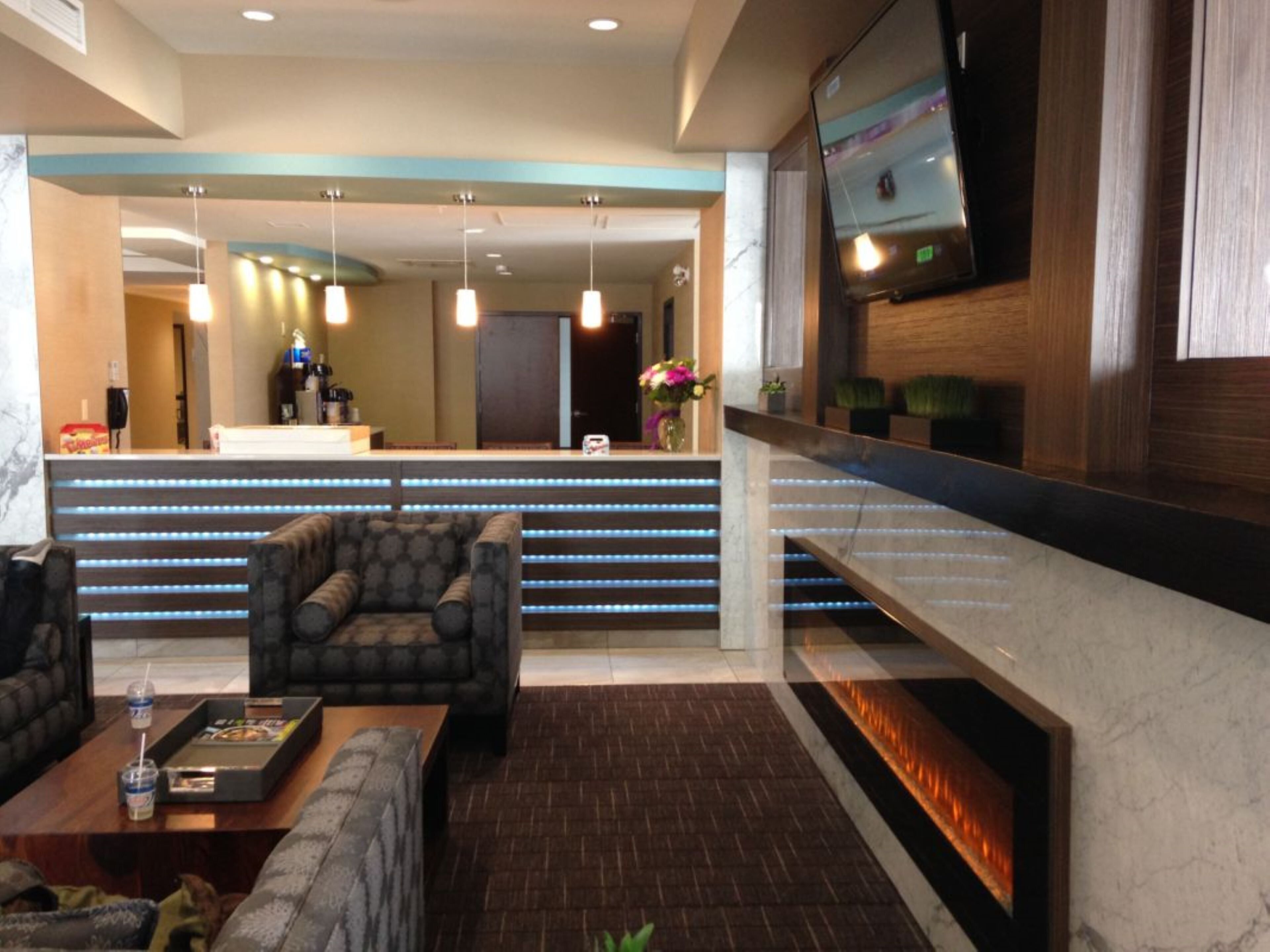 A hotel lobby with a reception desk, seating area, and a flat-screen TV mounted on the wall.
