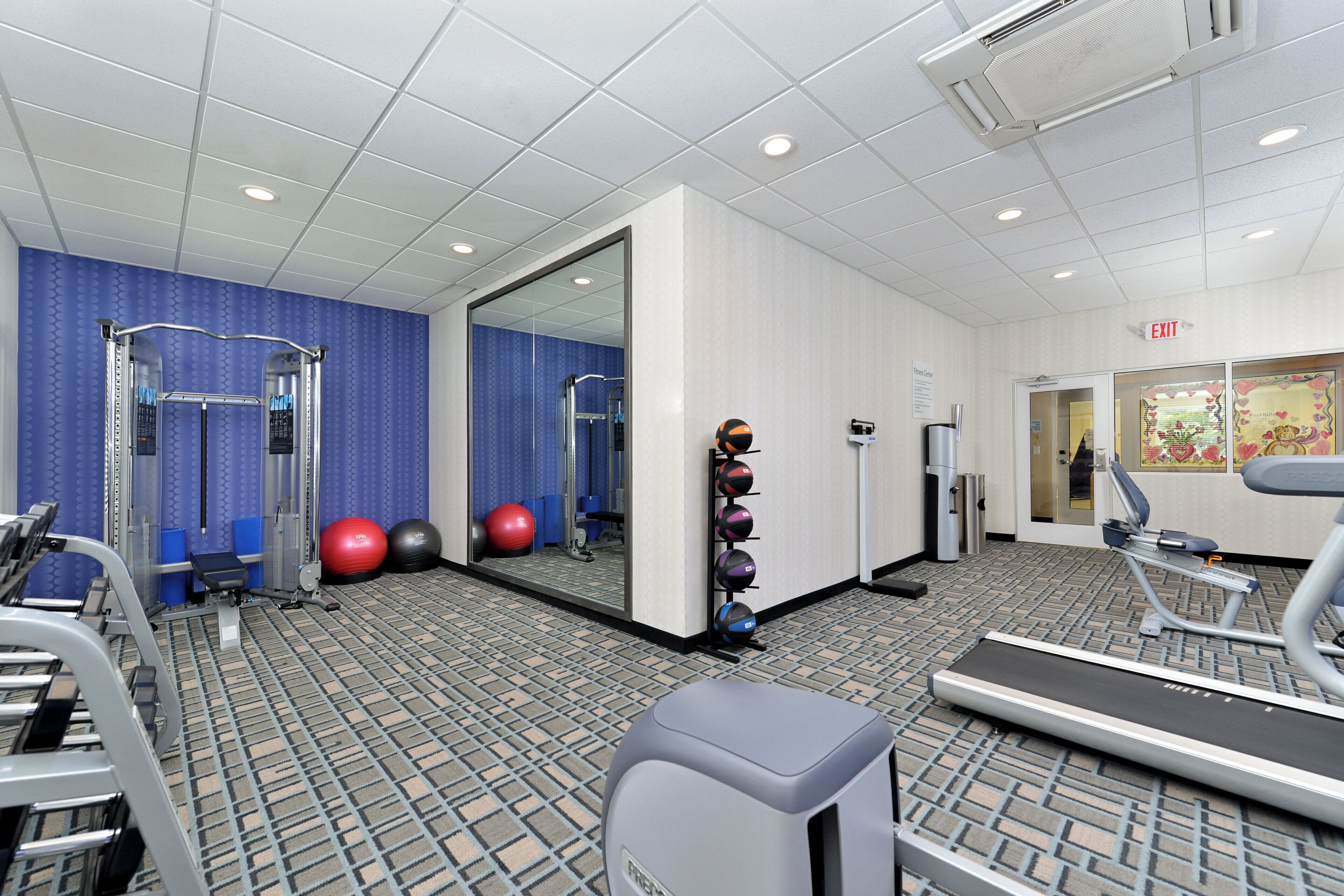A fitness center with exercise equipment, a mirrored wall, and a patterned floor.