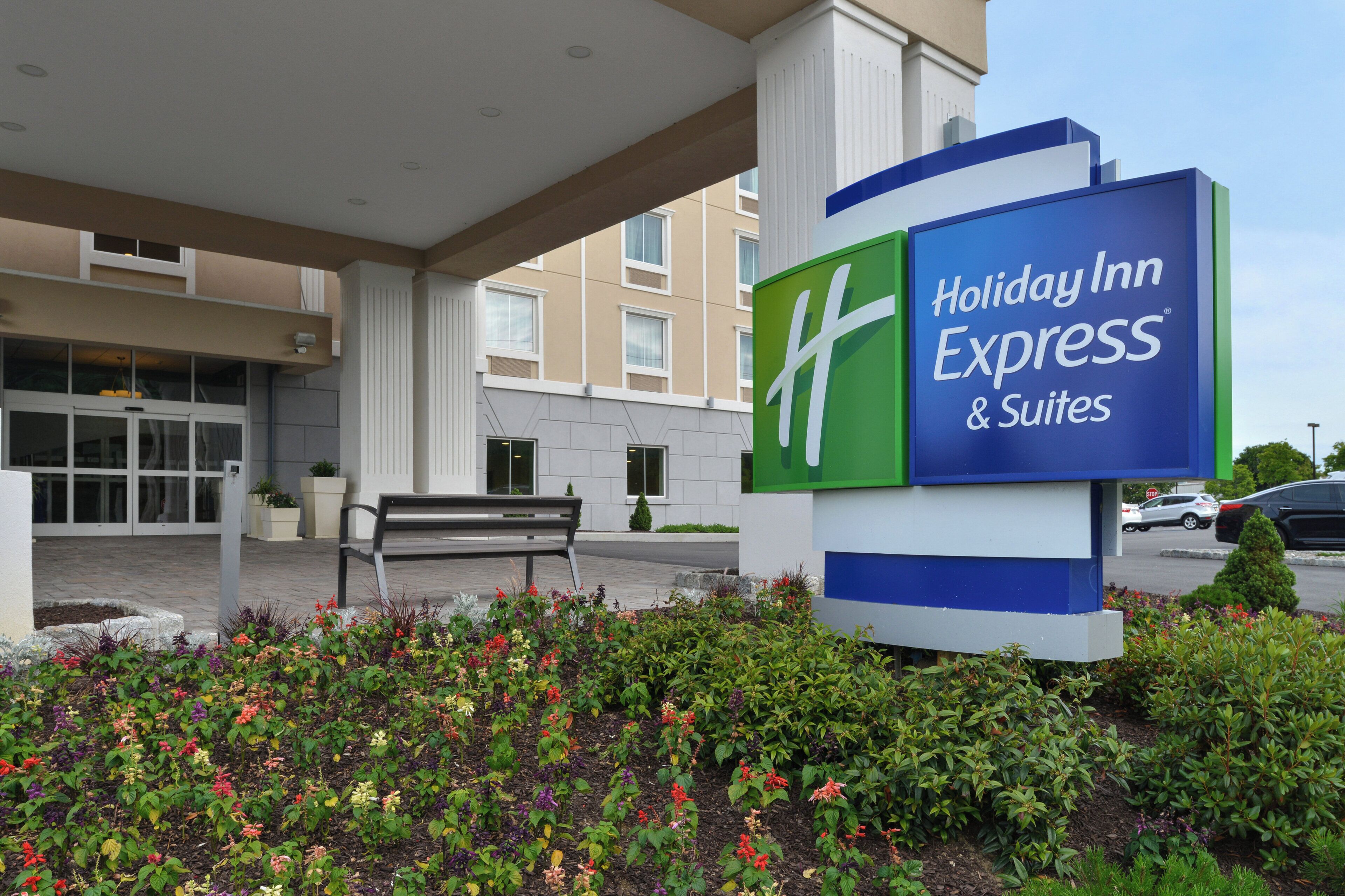 A Holiday Inn Express & Suites sign with a bench and flower beds in front.