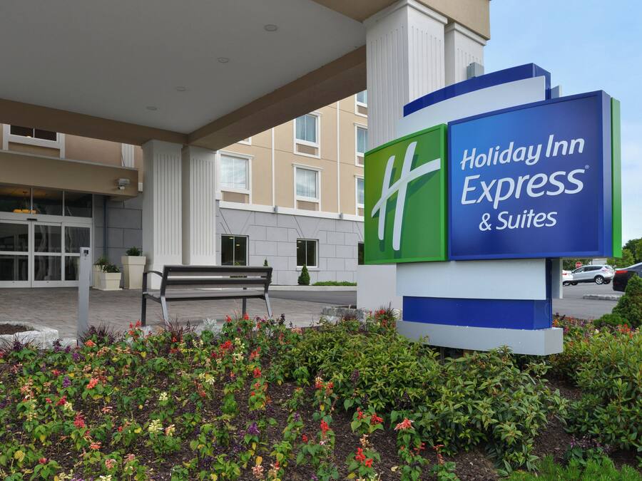 Segnaletica Holiday Inn Express & Suites con una panchina e aiuole fiorite di fronte.