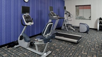 Un gimnasio con equipo de cardio, un reloj de pared y una ventana con persianas.