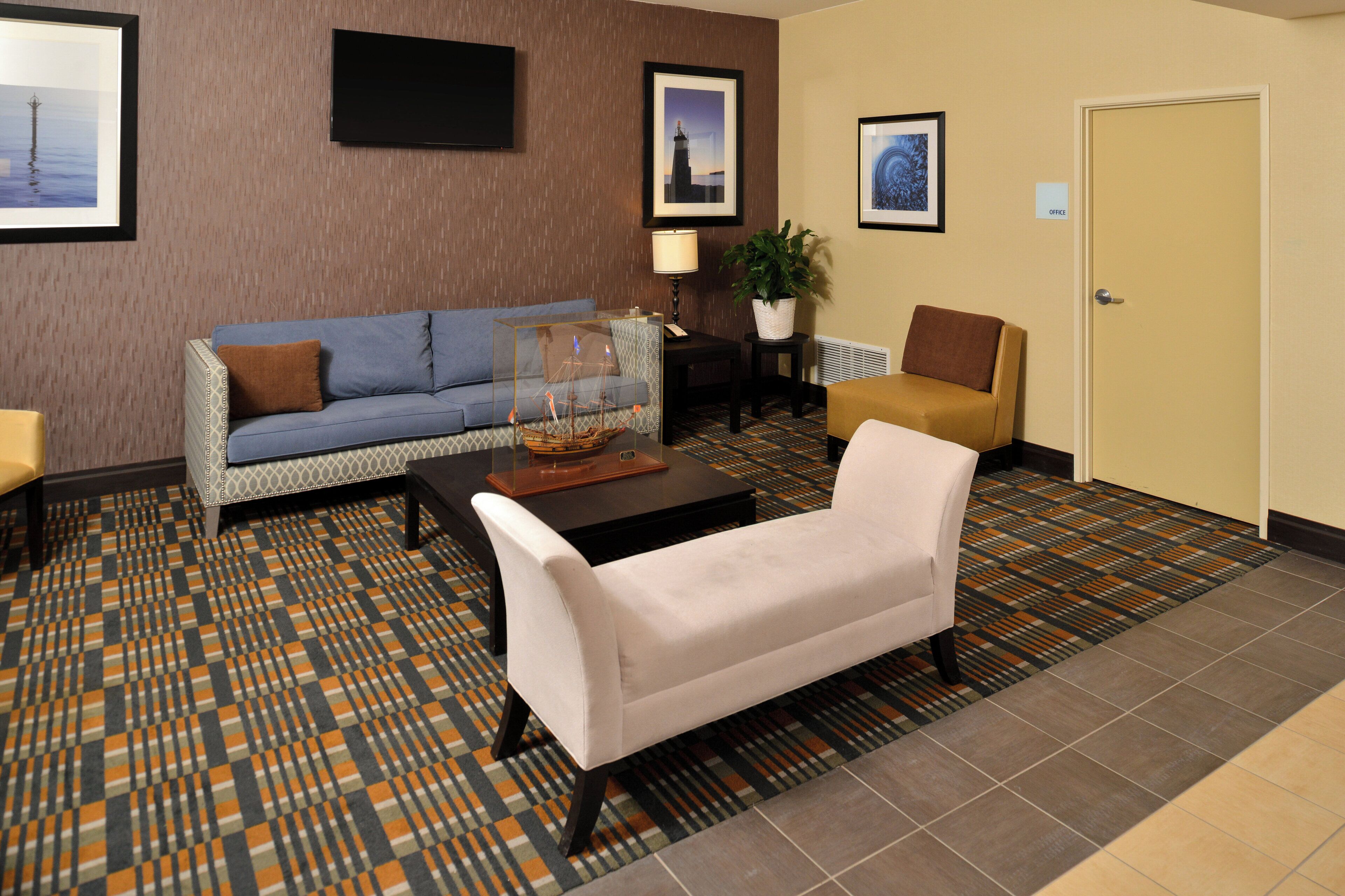 A hotel lobby with a blue sofa, a white armchair, a coffee table, and a patterned carpet.