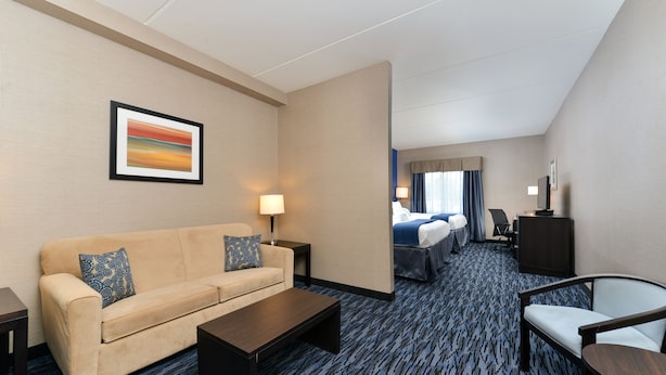 A hotel room with a sofa, a coffee table, a TV, a desk, and a bed. - Holiday Inn Express & Suites Peekskill-Lower Hudson Valley by IHG (Peekskill)