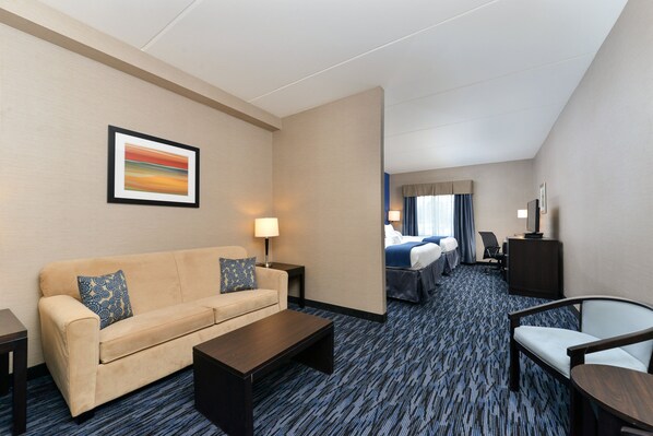 A hotel room with a sofa, a coffee table, a TV, a desk, and a bed.
