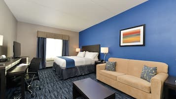 A hotel room with a bed, a desk, a chair, a sofa, and a coffee table.