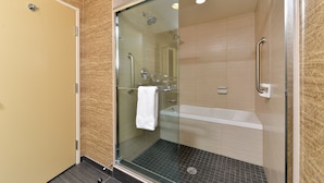 A glass-enclosed shower with a white towel hanging on the door handle, a handheld showerhead, and a handheld showerhead mounted on the wall. - Holiday Inn Express & Suites Peekskill-Lower Hudson Valley by IHG (Peekskill)