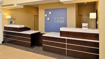 Zona de recepción de hotel con dos mostradores, una pared azul con el logotipo de Holiday Inn Express y un cartel que indica la oficina.