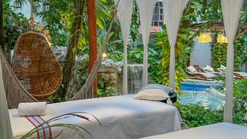 A cozy outdoor lounge area with two beds, a hanging light fixture, and a view of a pool.