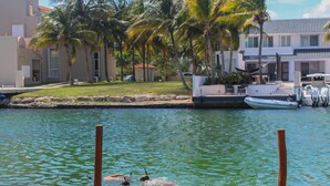 A waterfront property with a dock, a boat, and palm trees. - Chez Waffle Hotel  (Puerto Aventuras)