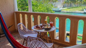 A balcony with a table set for dining, chairs, and a hammock. - Chez Waffle Hotel  (Puerto Aventuras)