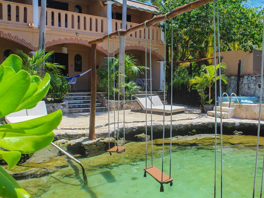 Un área de piscina con un conjunto de columpios, sillas de descanso y un muro de piedra.