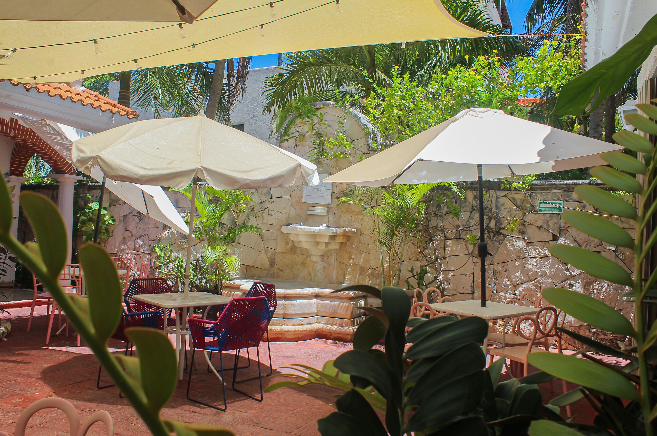 Une terrasse extérieure avec des tables, des chaises et des parasols, entourée de plantes et d’un mur en pierre.
