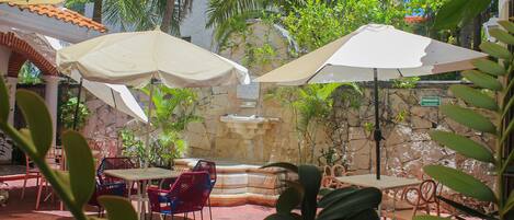 An outdoor patio with tables, chairs, and umbrellas, surrounded by plants and a stone wall.