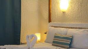 A hotel room with a neatly made bed, a pillow with a geometric pattern, and a wall-mounted light fixture. - Chez Waffle Hotel  (Puerto Aventuras)