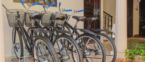 Three bicycles parked outside a building with a tiled floor and a metal fence.