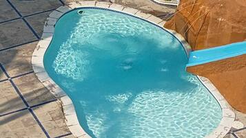 Une piscine dont le bord est revêtu de carrelage, entourée d’une terrasse en pierre.