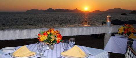 A table set for two with a view of the sunset over the sea.
