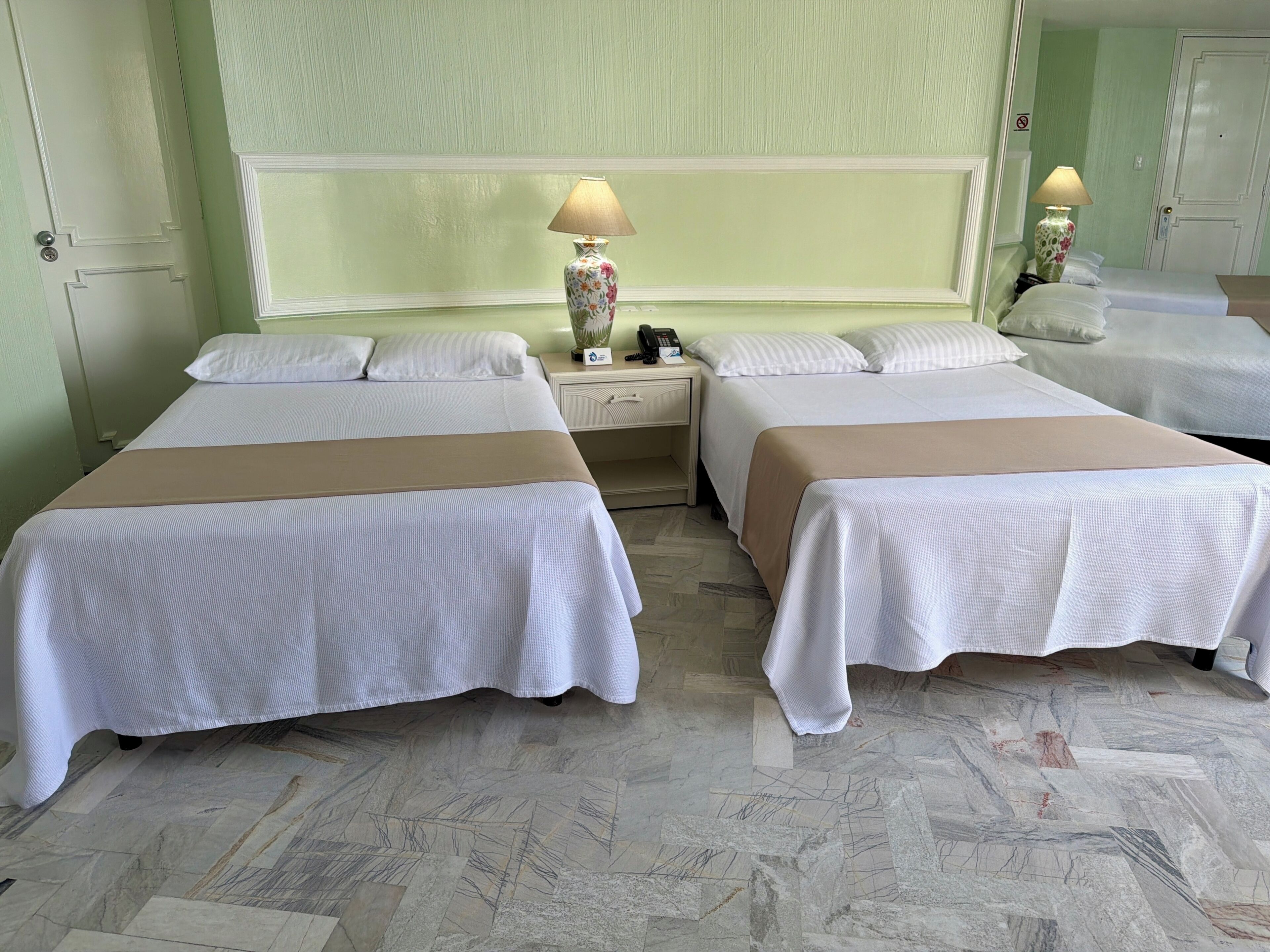 A hotel room with two beds, a nightstand with a lamp, and a mirror.