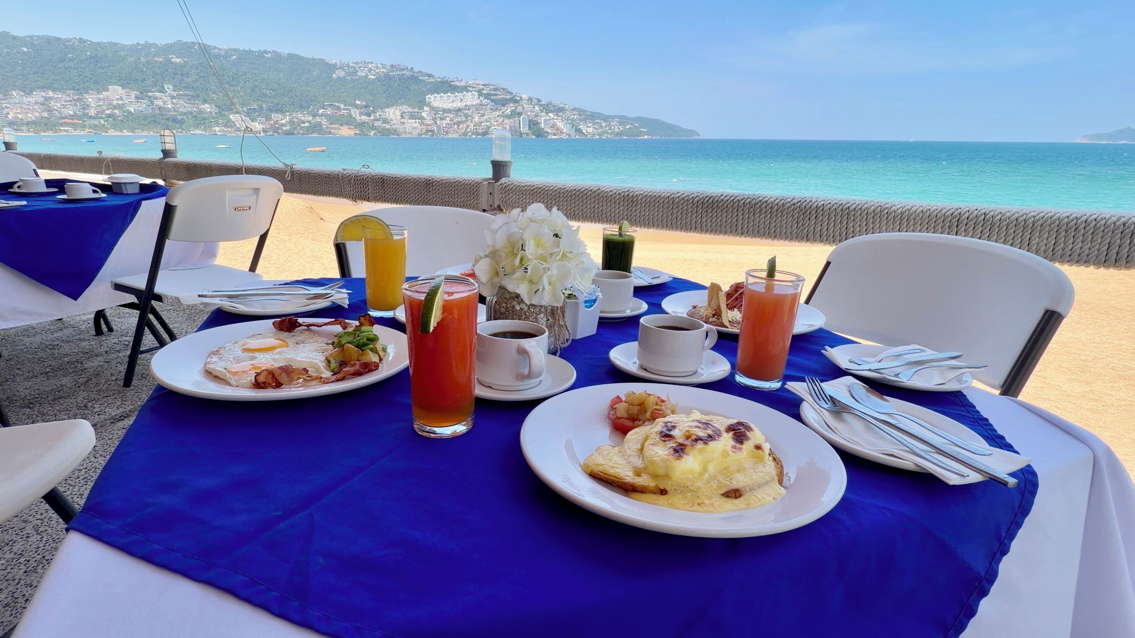 A table set with breakfast items, including eggs, toast, and beverages, overlooking a coastal view.