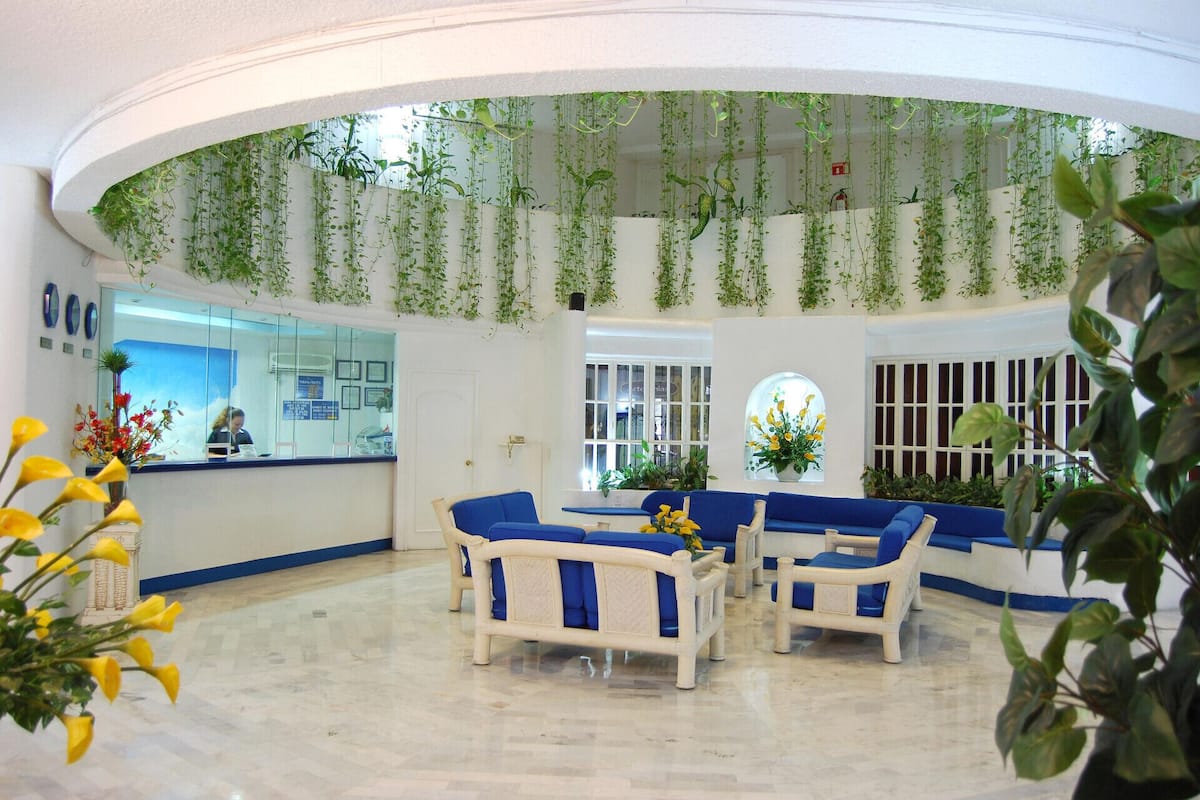 Un vestíbulo con techo curvo, plantas colgantes, mostrador de recepción y mobiliario azul y blanco.