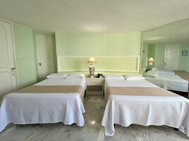 Habitación de hotel con dos camas, un espejo grande y una mesita de noche con lámpara.
