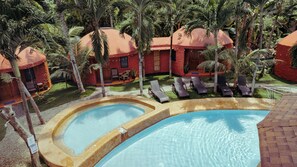 A pool area with lounge chairs and a hot tub, surrounded by palm trees and red-roofed buildings. - Panglao Chocolate Hills Resort (Dauis)
