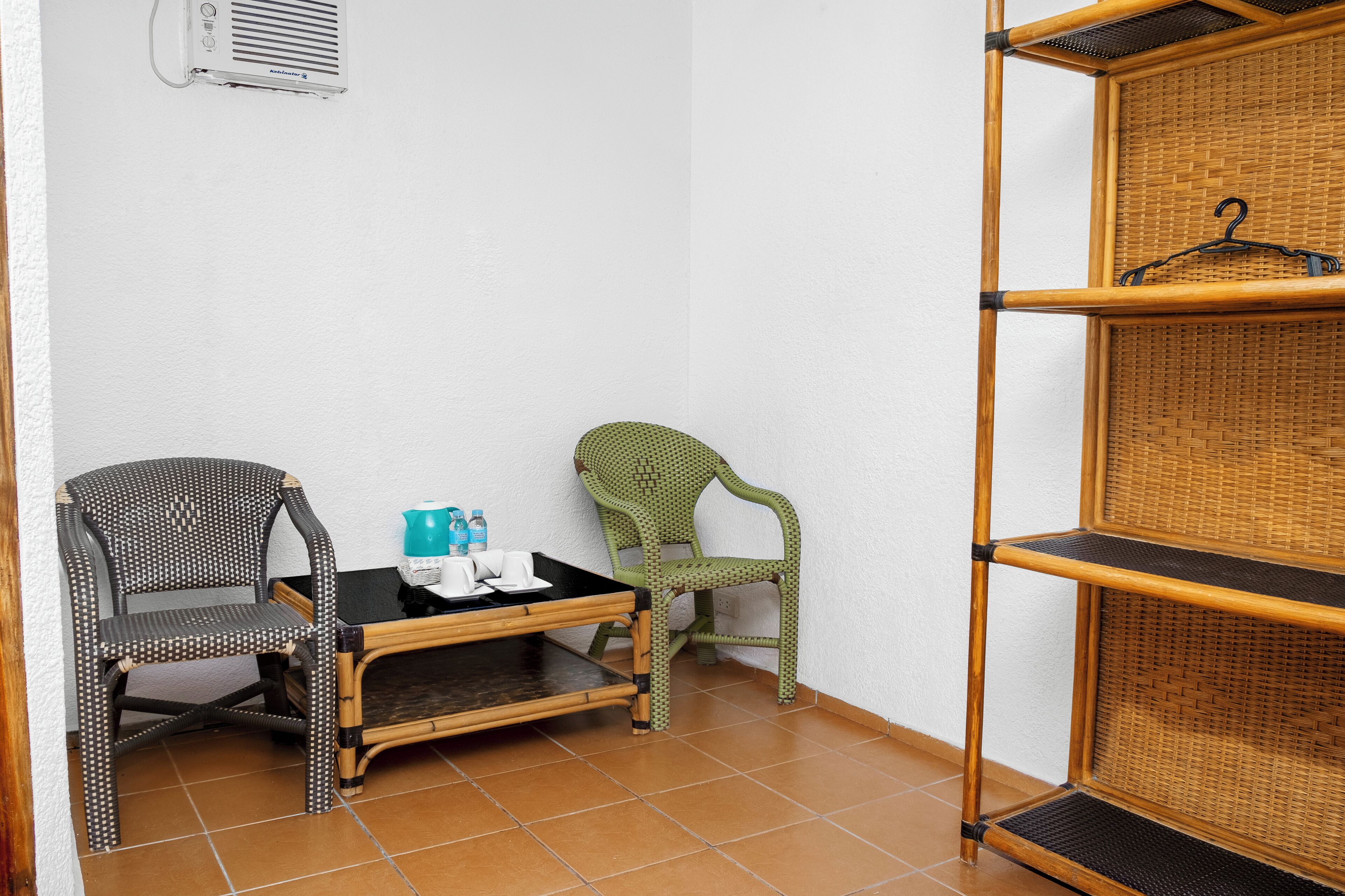 Habitación de esquina con dos sillones, una mesita, una estantería y aire acondicionado instalado en la pared.