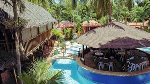Ein Resort mit Schwimmbad, Sitzgelegenheiten im Freien und strohgedeckten Gebäuden.