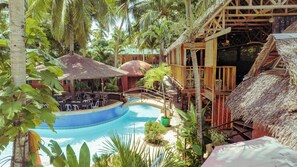 A pool area with a thatched-roof structure, surrounded by lush greenery and a wooden deck. - Panglao Chocolate Hills Resort (Dauis)