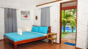 Ein Zimmer mit einem Bett, einem kleinen Tisch, einem Gemälde und Blick auf einen Strand.