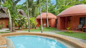 A pool surrounded by thatched-roof cottages with a well-maintained lawn and tropical plants. - Panglao Chocolate Hills Resort (Dauis)