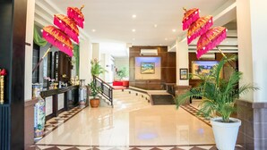 Een hotel lobby met een receptiebalie, een trap en potplanten.