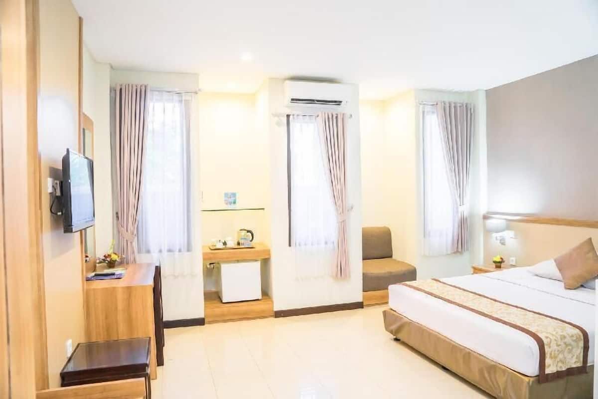 A hotel room with a bed, a desk, a chair, a TV, an air conditioning unit, and curtains.