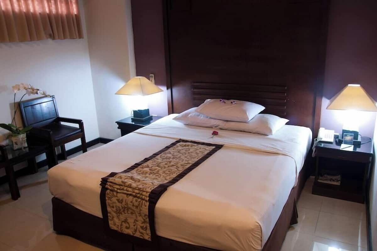A hotel room with a large bed, two bedside tables, a desk with a chair, and a window with curtains.