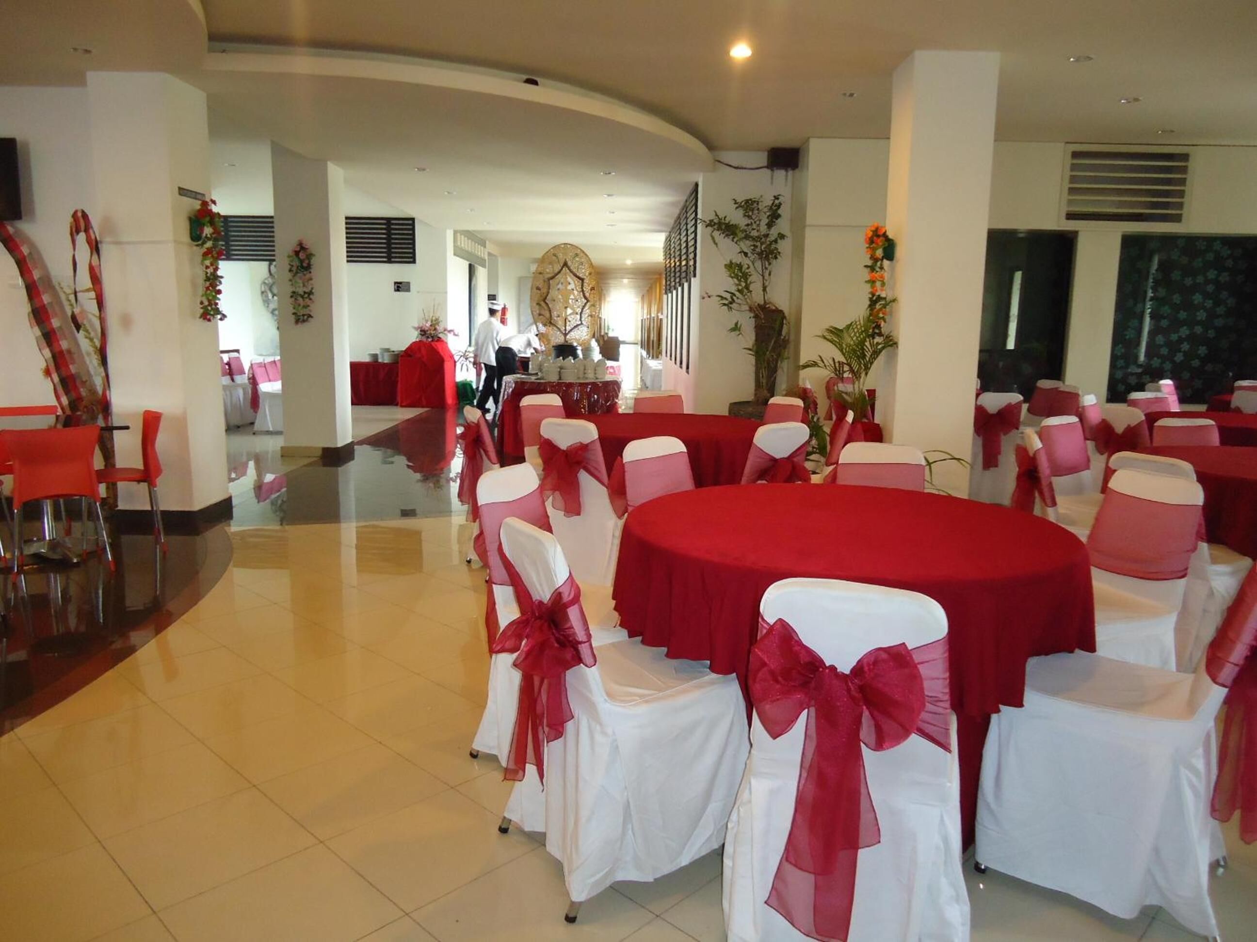 Un salón de banquetes con mesas redondas cubiertas con manteles rojos y sillas blancas adornadas con cintas rojas.