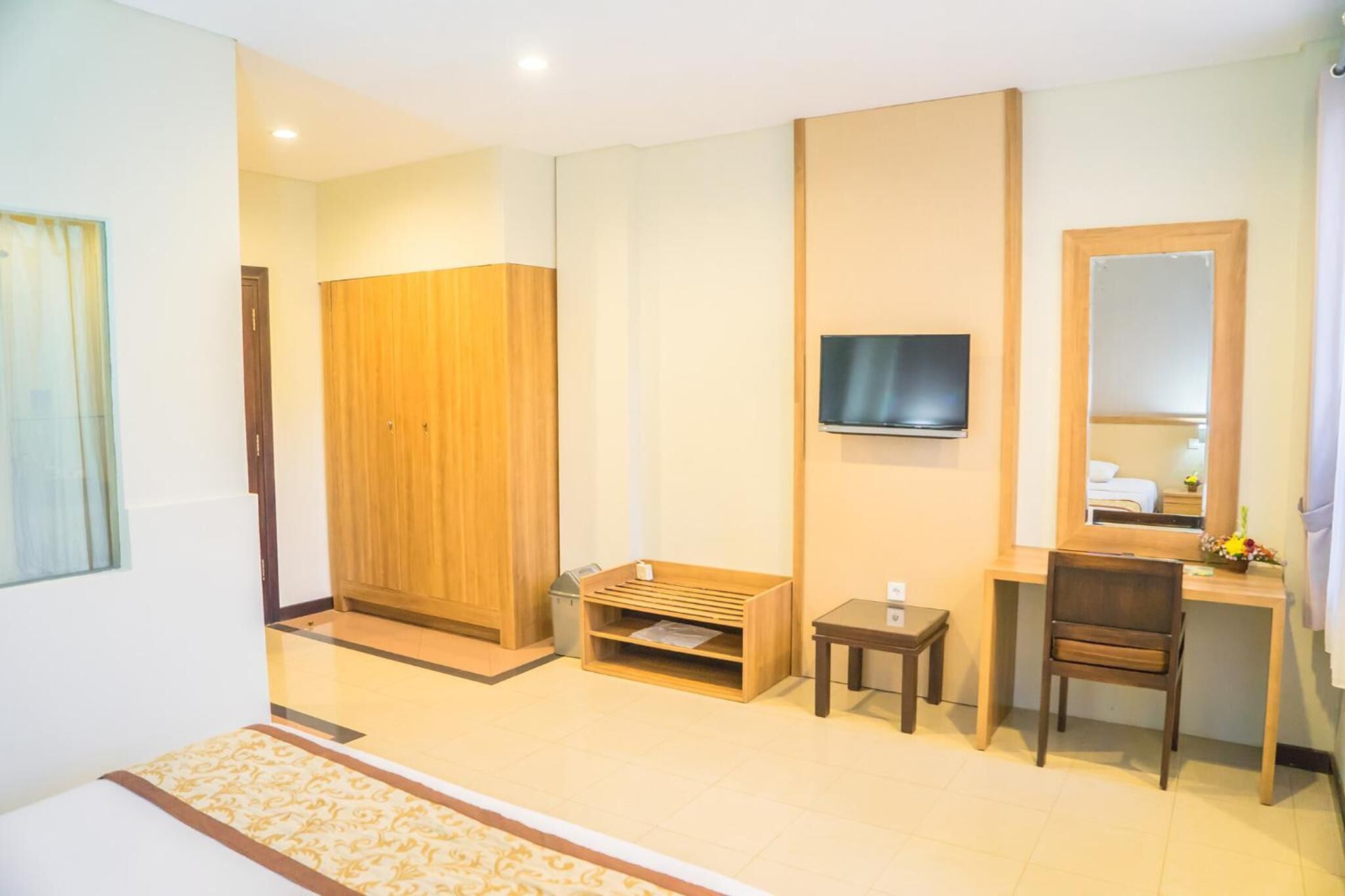 A hotel room with a bed, a wooden wardrobe, a desk with a chair, a television, and a mirror.