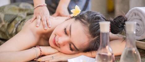 A person receiving a massage in a room with a bed, a tray with bottles, and a flower.